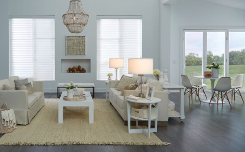 A white and tan-colored living area with a couch, loveseat, and shades lowered.