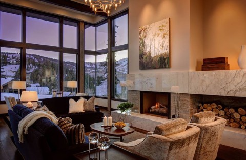 A living room with a fireplace, chandelier, accent lighting, and picture windows overlooking mountains.