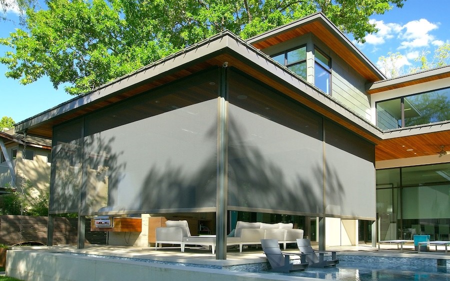 A pool and patio area of a modern home with motorized shades partially lowered around the seating area.